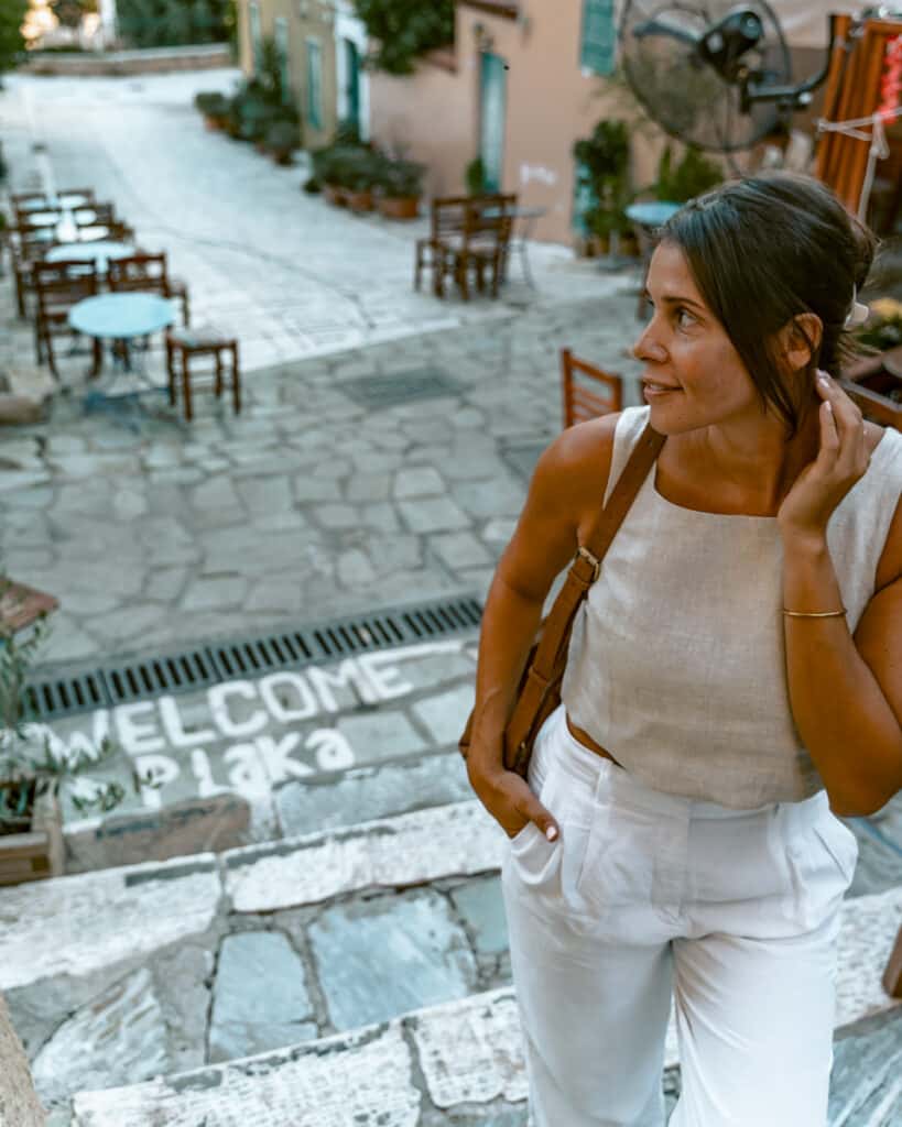 Me walking through Plaka’s cobblestone streets lined with cafes and pastel-colored houses, with “Welcome to Plaka” painted on the steps.