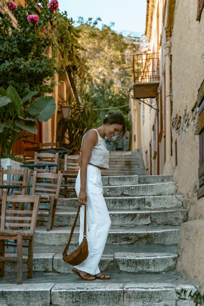 Me in white linen pants and sandals walking down narrow stone steps in Plaka neighborhood beneath the Acropolis.
