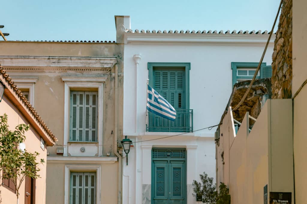 A Greek flag hanging proudly from the balcony of a whitewashed building with turquoise shutters in Plaka. A small but iconic detail you’ll notice while exploring Athens in 2 days.