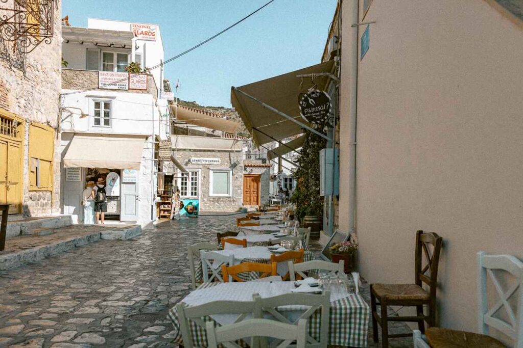 Square in Hydra lined with a tables and chairs at a taverna and souvenir shops.