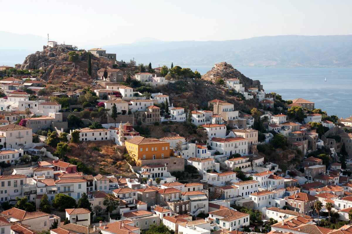 Scenic hillside view of whitewashed houses with terracotta roofs on Hydra island, captured during an Athens to Hydra day trip, with the Aegean Sea in the background.