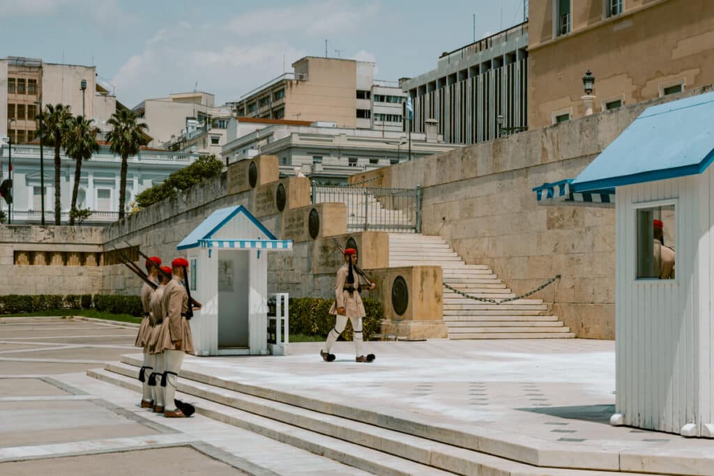 Traditional Evzones guards in beige uniforms and red caps performing the ceremonial change of the guard in front of the Greek Parliament at Syntagma Square. A cultural ritual that makes Athens worth visiting.