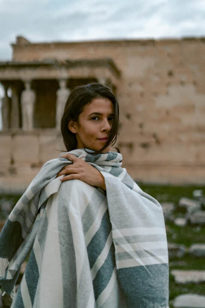 Me wrapped in a striped blanket standing near the Erechtheion temple at the Acropolis in Athens, with the Caryatid statues in the background. A cozy moment showing the quieter, reflective side of visiting Athens.