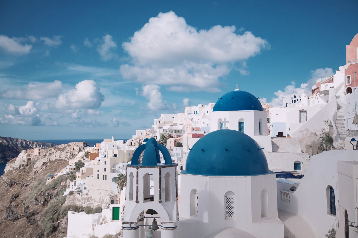 Whitewashed buildings and iconic blue-domed churches overlooking the cliffs of Santorini under a bright blue sky, a scene often featured in Greece Instagram captions for its postcard-perfect beauty.