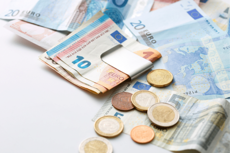 Euro banknotes and coins spread across a white surface, representing travel costs for visitors wondering if Athens is expensive.