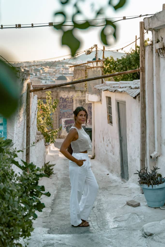 Woman standing in a quiet alley in Anafiotika, with whitewashed walls and city views in the background, capturing how simple neighborhood strolls can be one of the cheapest ways to enjoy Athens.