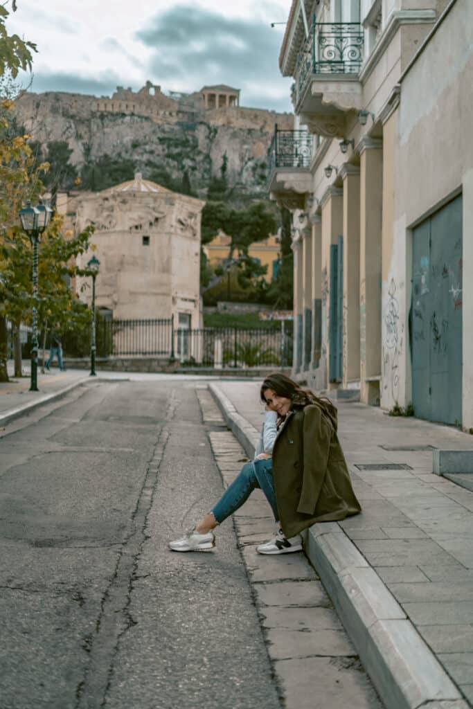 Me sitting on a curb in a quiet Athens street with the Acropolis visible on the hill behind her. A peaceful and safe moment in the city.