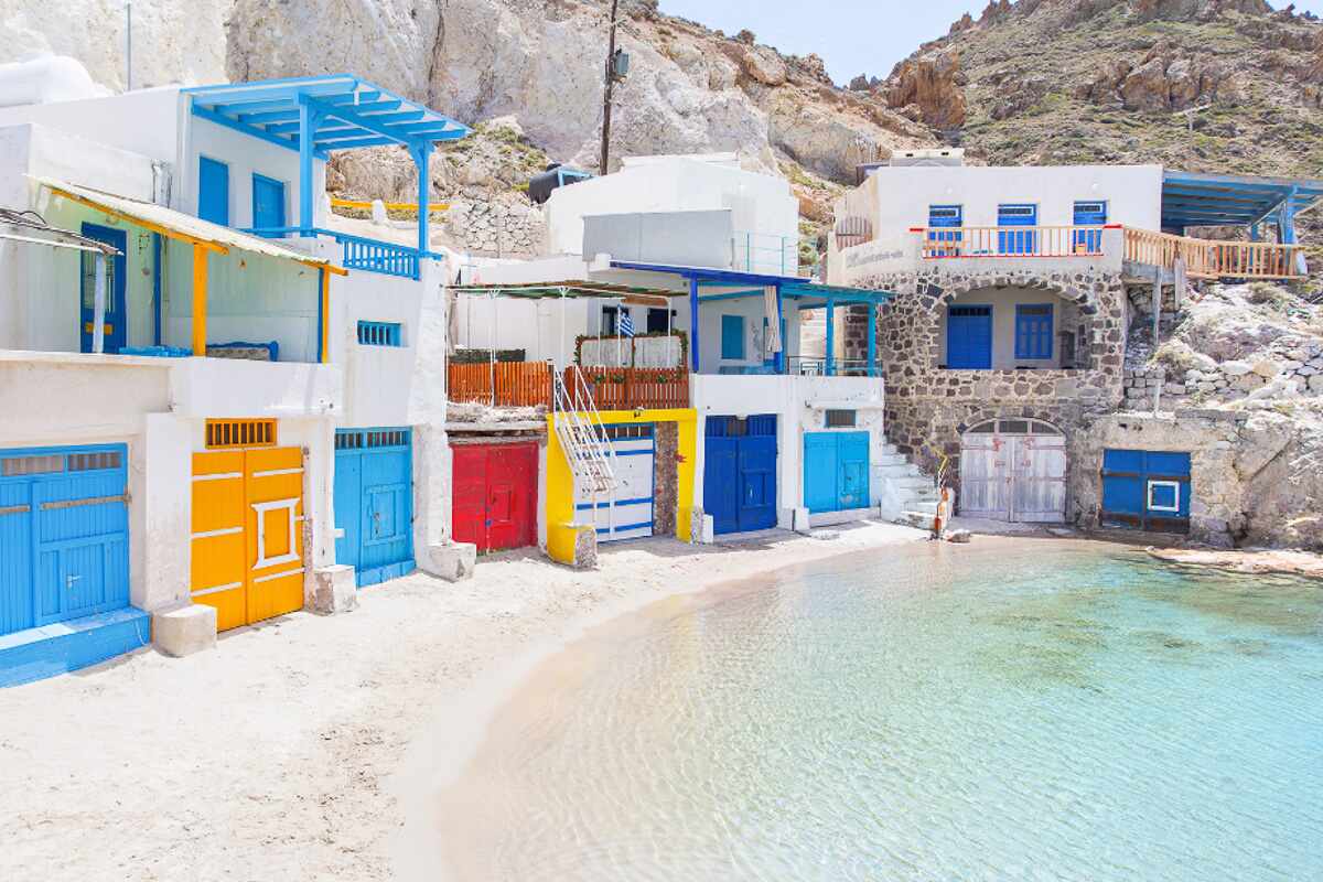 Colorful fishing houses with bright blue, yellow, and red doors lining the waterfront in Milos, Greece, showing the island charm travelers often seek when deciding what to buy in Greece as souvenirs.