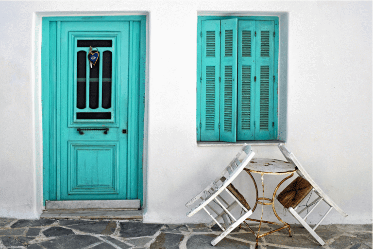 Traditional Greek island home with a turquoise door and shutters, whitewashed walls and outdoor seating, perfect inspiration for a 14 day Greece travel itinerary.