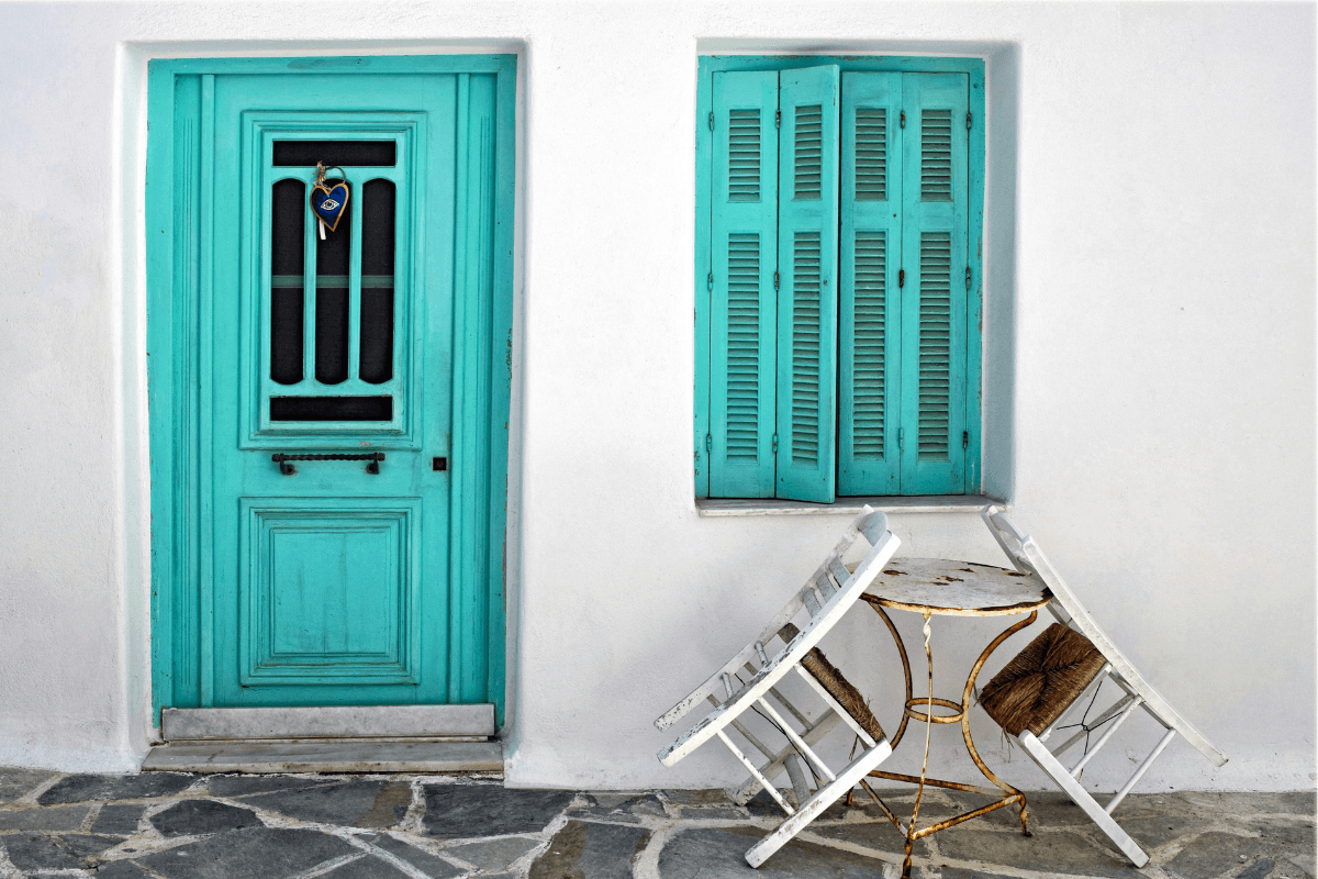 Traditional Greek island home with a turquoise door and shutters, whitewashed walls and outdoor seating, perfect inspiration for a 14 day Greece travel itinerary.