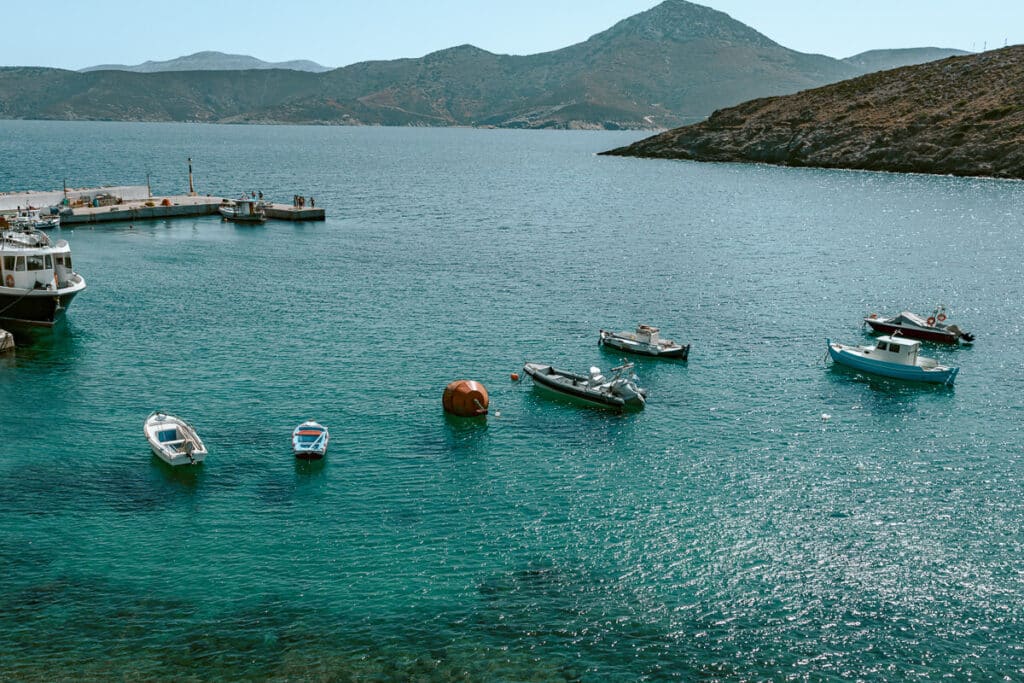 Several small fishing boats float in the sparkling turquoise water in Thymenia, with mountains in the distance
