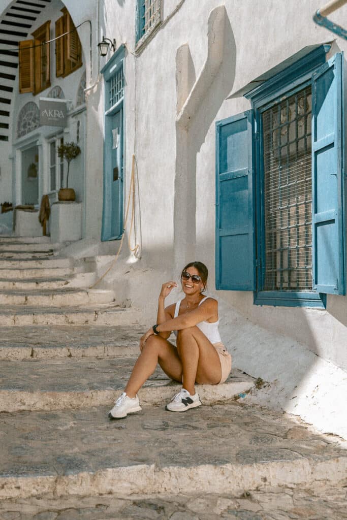 Me sitting on whitewashed stone steps with blue shutters and doors, enjoying the sunshine in Hydra.