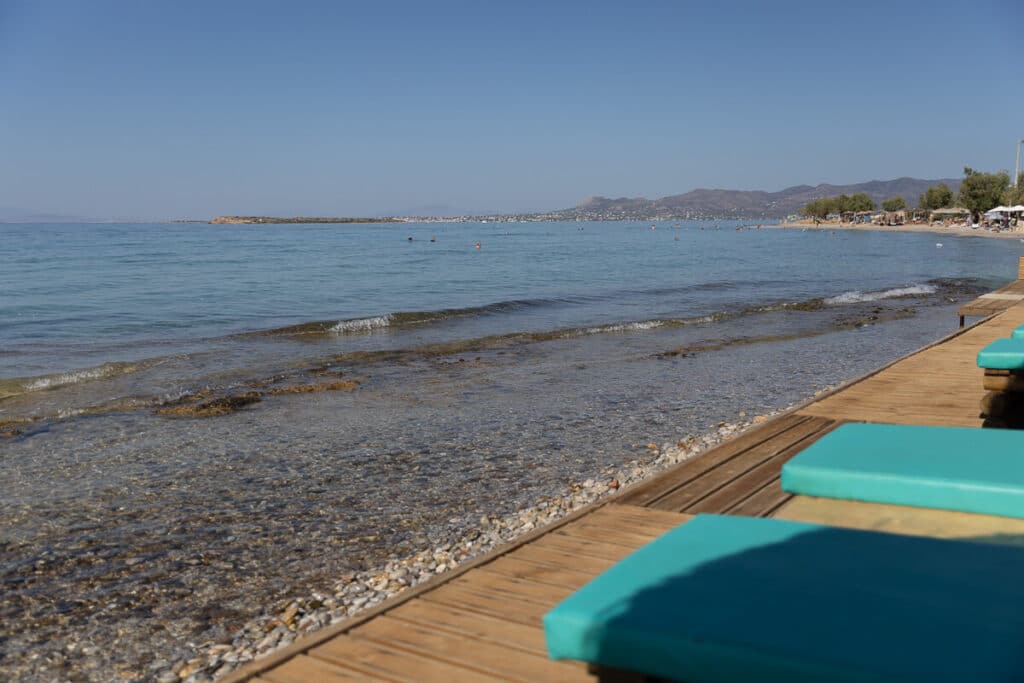 Beachfront view with turquoise sunbeds along the pebbled shore in Agistri, overlooking calm blue waters.
