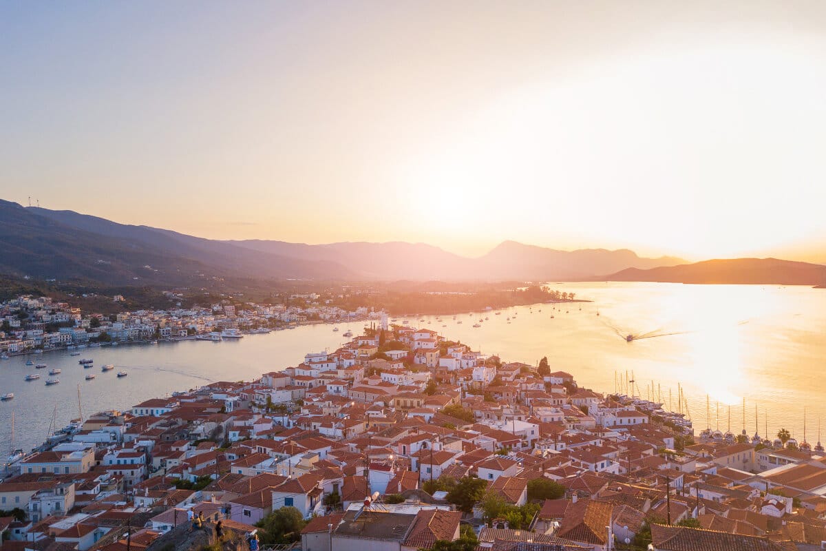 Sunset over Poros island with red-roofed houses and boats in the harbor, the perfect cover image for island day trips from Athens.