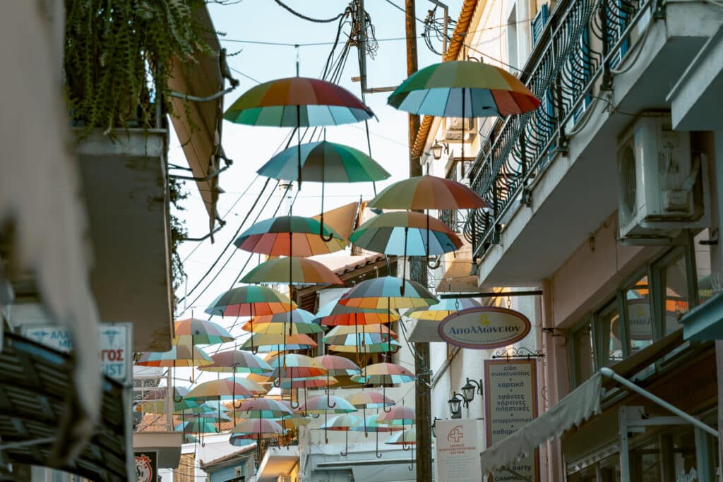 Row of colorful umbrellas strung across a street, creating a playful canopy above shops and balconies.