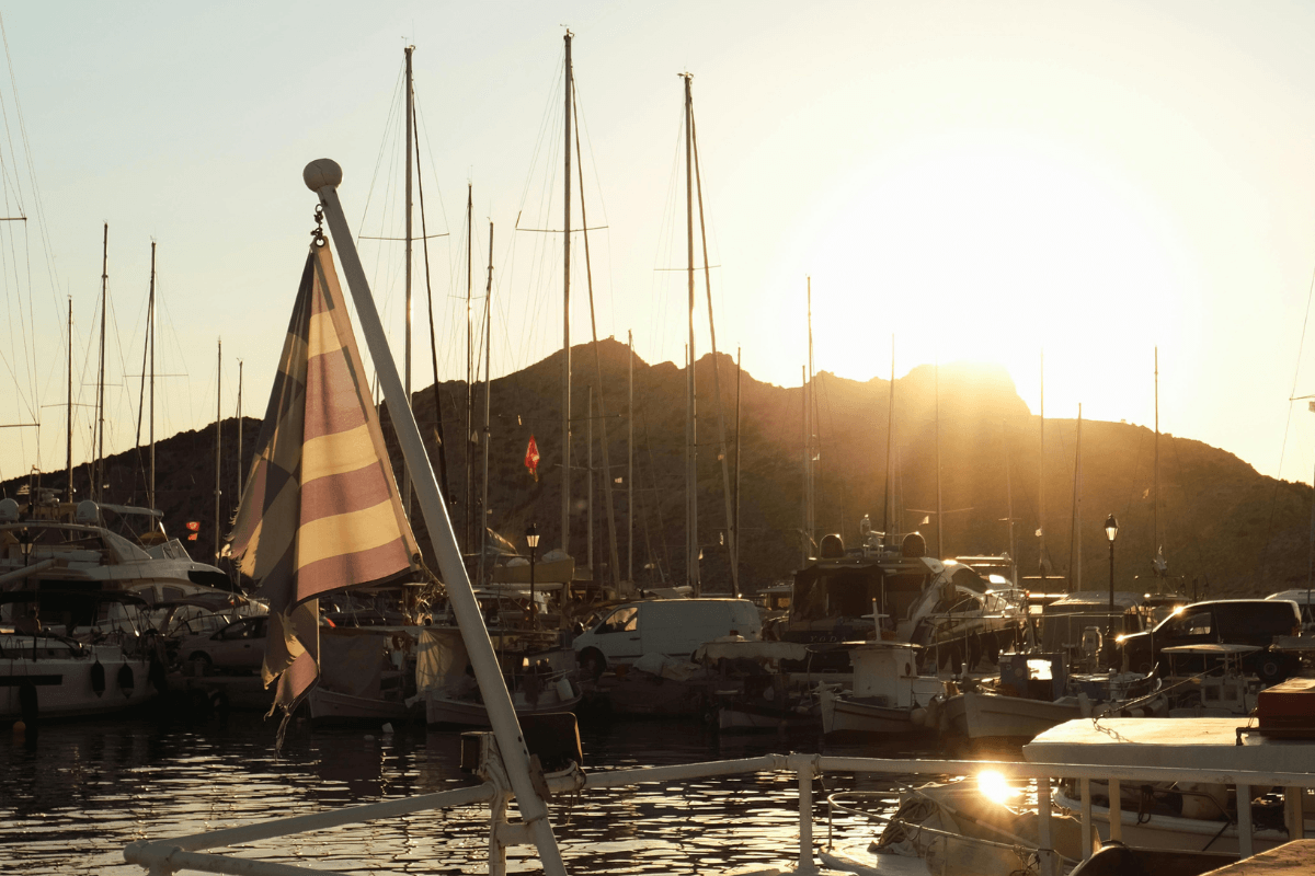 Sailboats and yachts docked in a Greek island harbor at sunset, capturing the scenery travelers can experience on island day trips from Athens.
