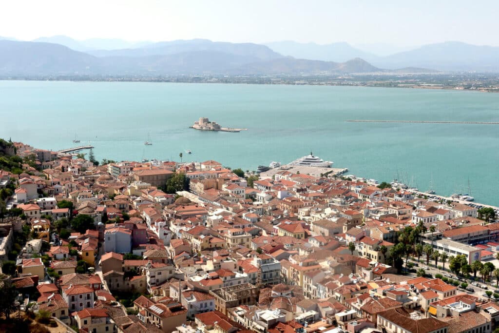A stunning aerial shot of Nafplio’s red-tiled rooftops stretching to the turquoise bay, with Bourtzi Castle floating just offshore, showcasing exactly what to do in Nafplio, Greece for epic views and local history.