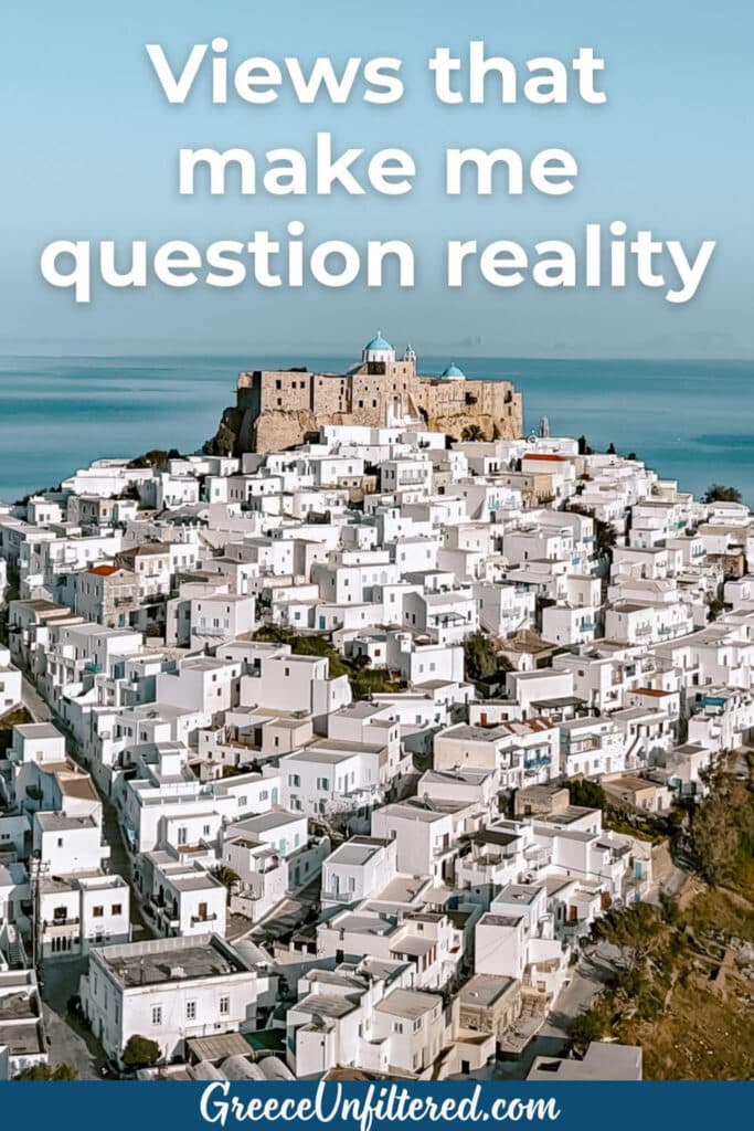 An epic aerial view of a Greek island’s white houses spilling down to the Aegean, with a castle rising above and the words “Views that make me question reality.” Ideal for Greek island captions that showcase breathtaking scenery.