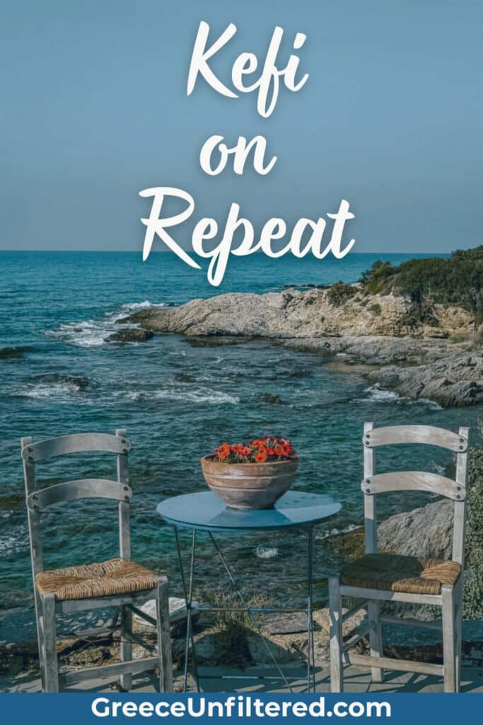 Two rustic wooden chairs and a blue table with a pot of flowers sit by the rocky shoreline on a Greek island, with “Kefi on Repeat” overlaid. This is perfect for anyone looking for uplifting Greek island captions about joy and simple pleasures.