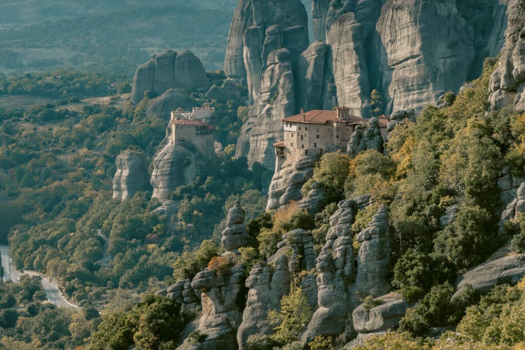 Panoramic shot of several Meteora monasteries dotting the ancient stone pillars, with layers of mountains fading into the distance.