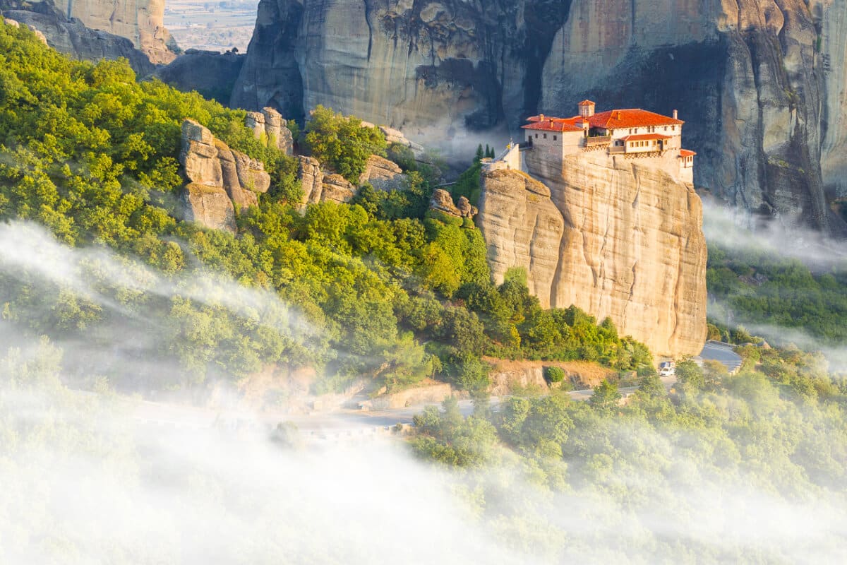 Meteora monastery floating above the morning mist, surrounded by bright green trees and towering rock faces for that otherworldly vibe and a must on any Meteora Guide.