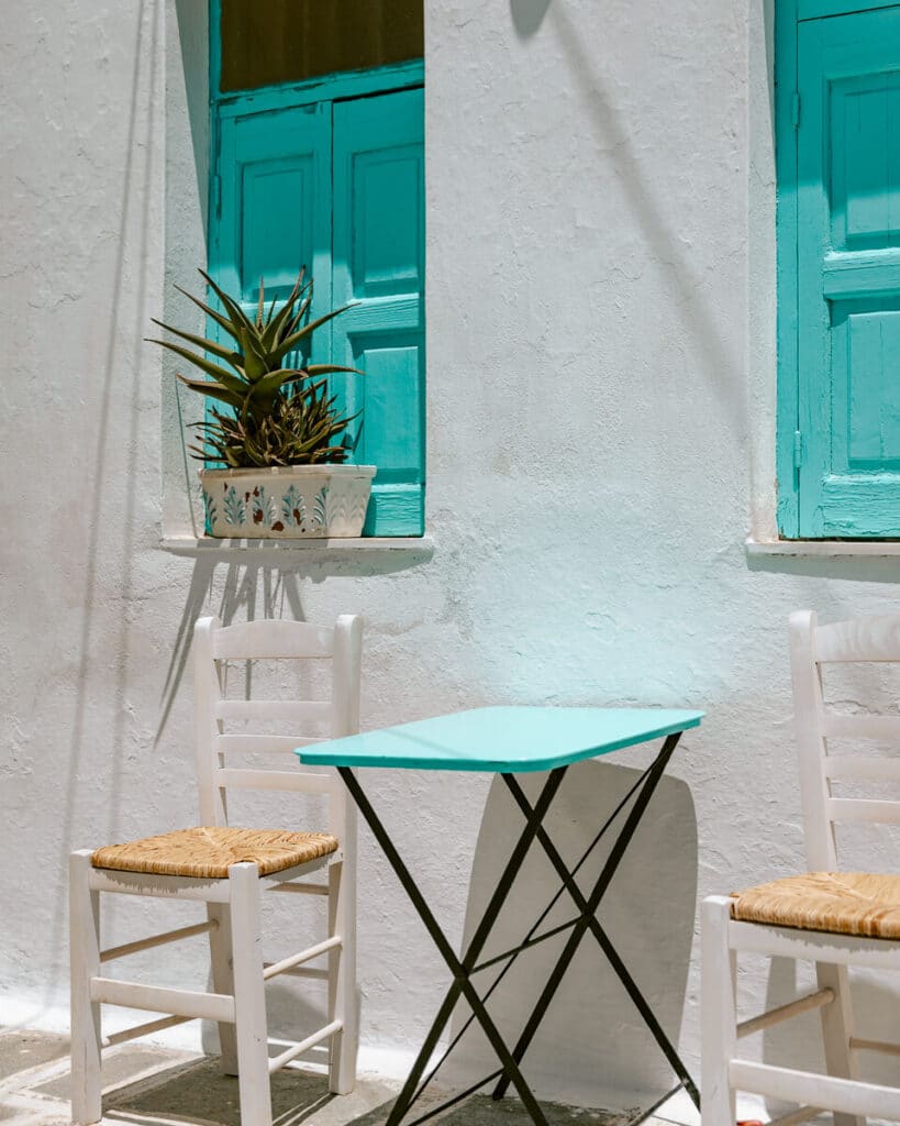 Simple turquoise table with two wooden chairs outside a whitewashed Serifos house — the perfect quiet Greek island moment.