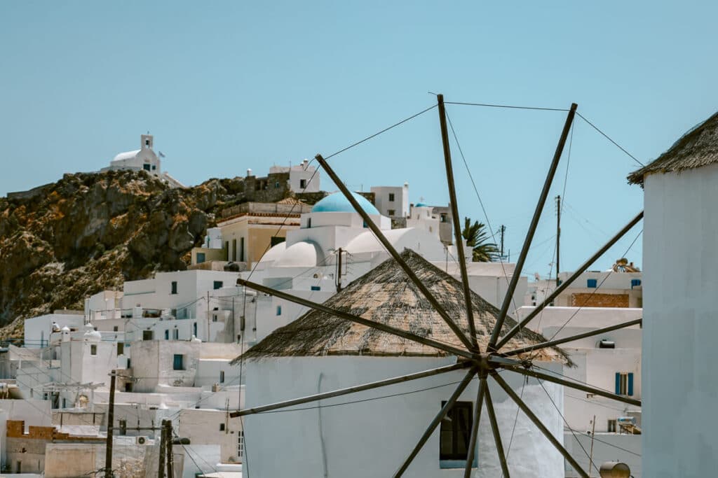 A rustic windmill in Chora, Serifos, framed by whitewashed houses with blue domes and the rocky hillside in the background.