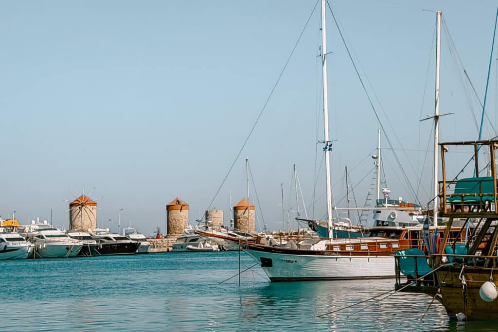 Boats in Mandraki Harbor with historic windmills in Rhodes, Greece.