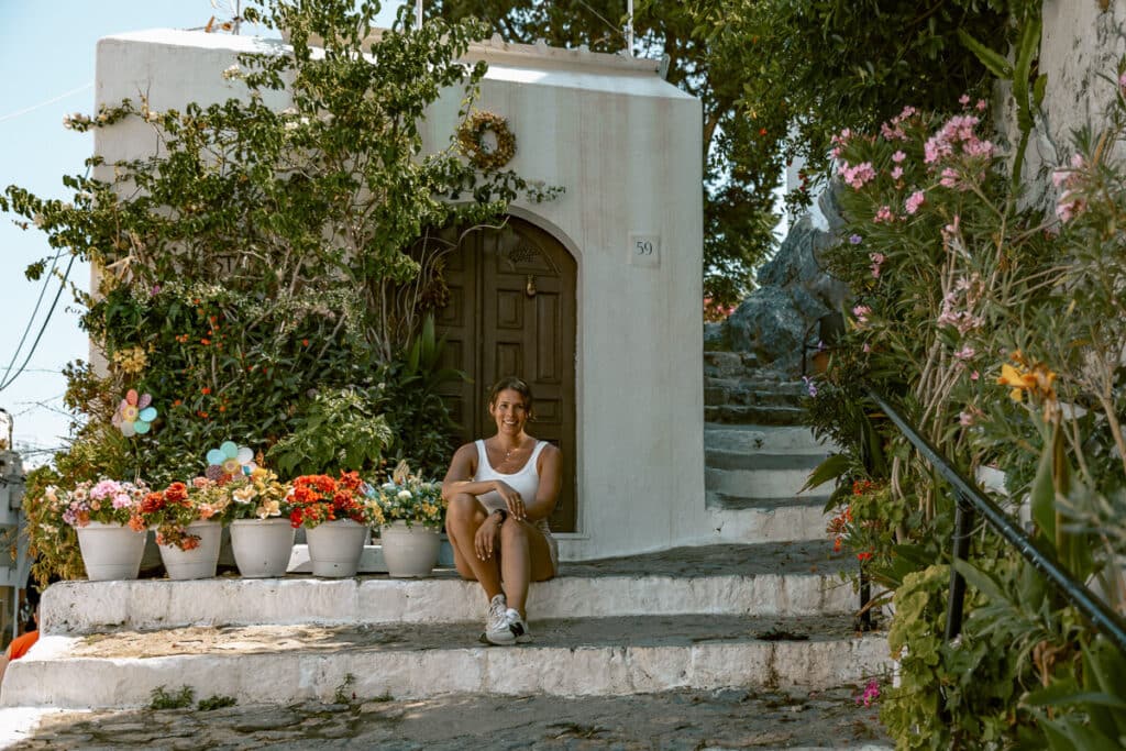 Woman sitting on whitewashed steps surrounded by flowers on the Greek island Rhodes.