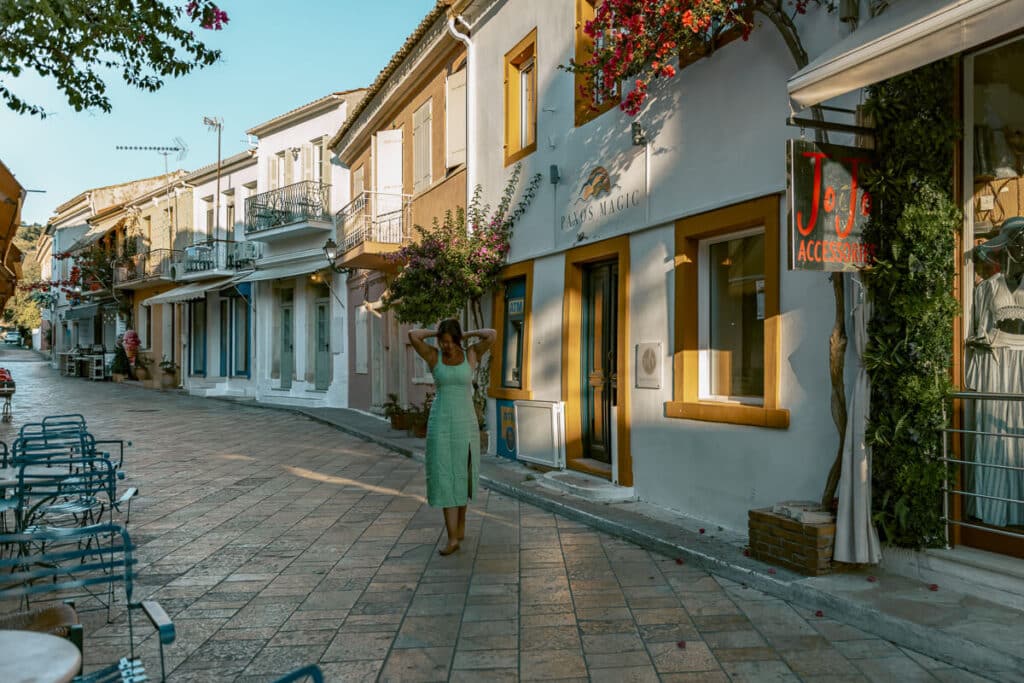 Woman walking through a charming street with shops and colorful buildings in Paxos, Greece.
