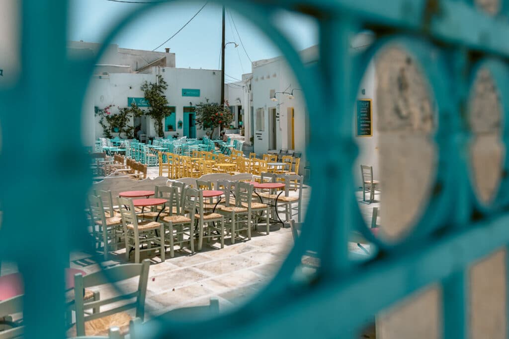 A charming Greek courtyard in Serifos filled with colorful chairs and tables viewed through a blue gate