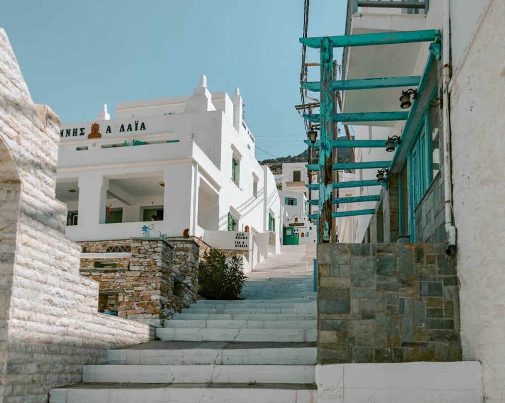 Stairway alley lined with classic Sifnos architecture, turquoise balconies, and taverna signs, showing how even the smallest streets reflect the island’s charm and authenticity.