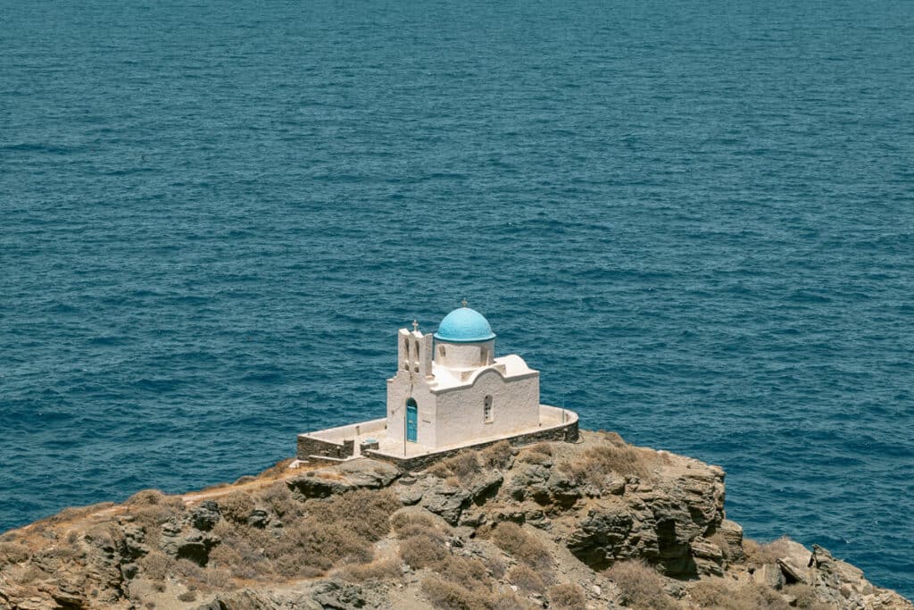 The Church of the Seven Martyrs perched on a rocky outcrop, its white walls and blue dome standing out against the vast Aegean Sea — one of the most iconic views that answers why Sifnos is worth visiting.