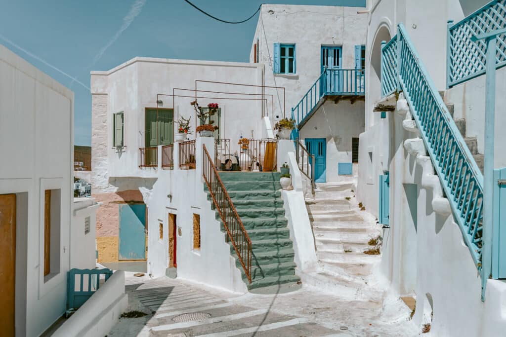Traditional Cycladic alleyway with colorful balconies, terracotta pots, and winding staircases.