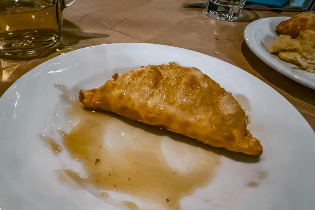 Fried pouggia cheese pie on a white plate in Astypalaia, served with a drizzle of honey at a local taverna.