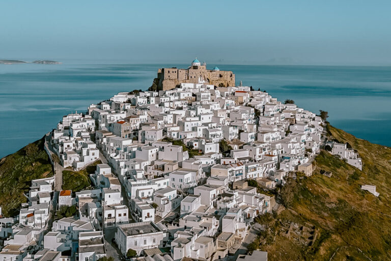 Drone view of Astypalaia’s castle perched on a hilltop, surrounded by tightly packed white homes and endless sea, this dramatic view is a must-see on any list of what to do in Astypalaia.