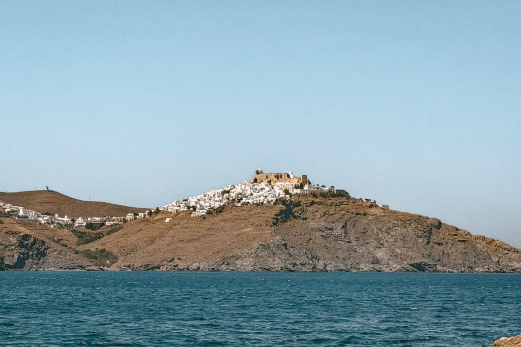 Distant view of Chora and Kastro in Astypalaia from across the sea, with whitewashed houses clustered on a rocky hill above the water.
