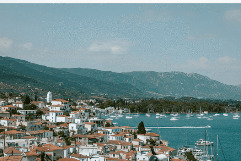 Coastal view of Poros with red roofed houses, sailboats in the harbor, and green mountains, a scenic stop on a day trip to Poros from Athens.