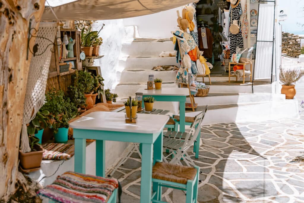 Outdoor café with turquoise tables and chairs along a whitewashed stone alley in Sifnos, Greece.