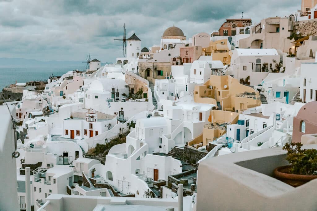 Whitewashed buildings and windmills in Oia, Santorini, under cloudy skies, showing the cliffside village views on a Greece itinerary.