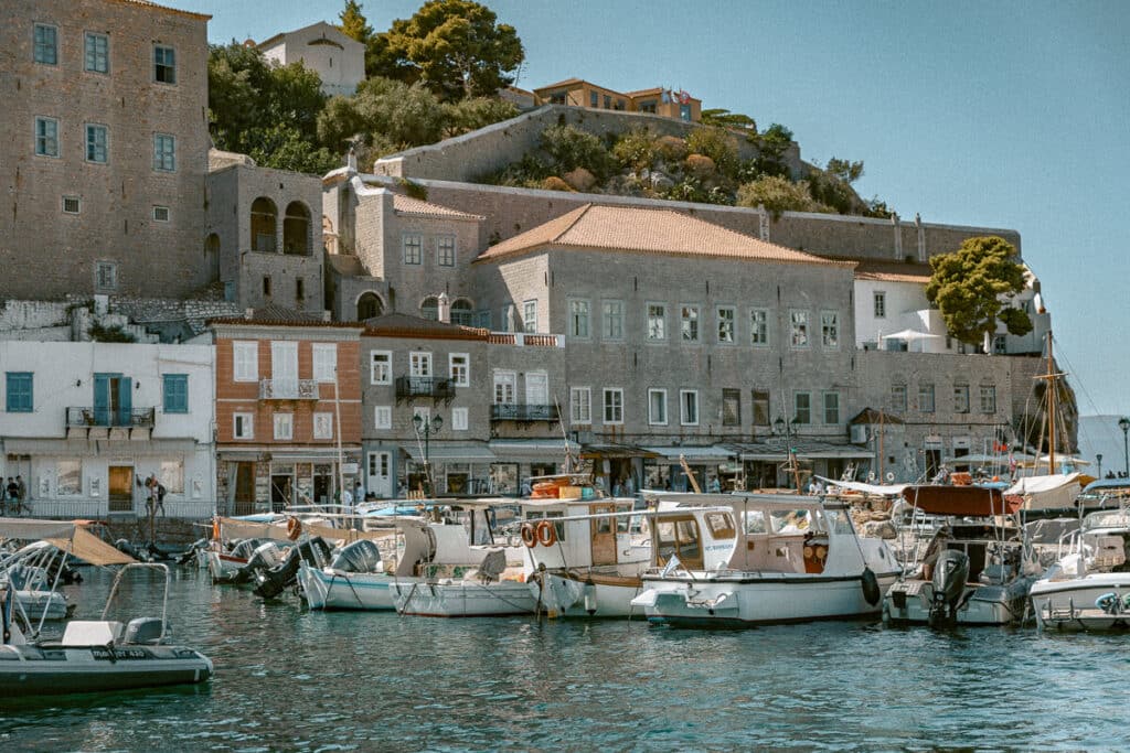 Fishing boats and traditional wooden vessels anchored in Hydra’s bustling port, with historic stone mansions towering behind. A view that blends seafaring heritage with Cycladic elegance, ideal for a Greece itinerary photo stop.