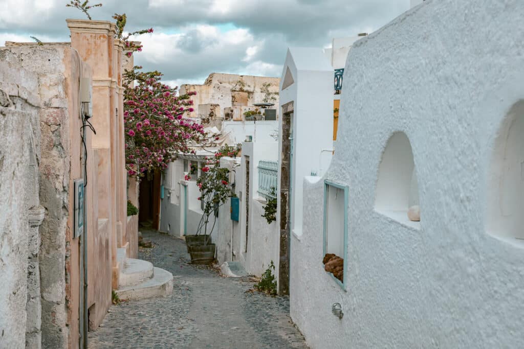Narrow pedestrian street in Santorini's winter off-season with shuttered shops and a clock tower under a partly cloudy sky