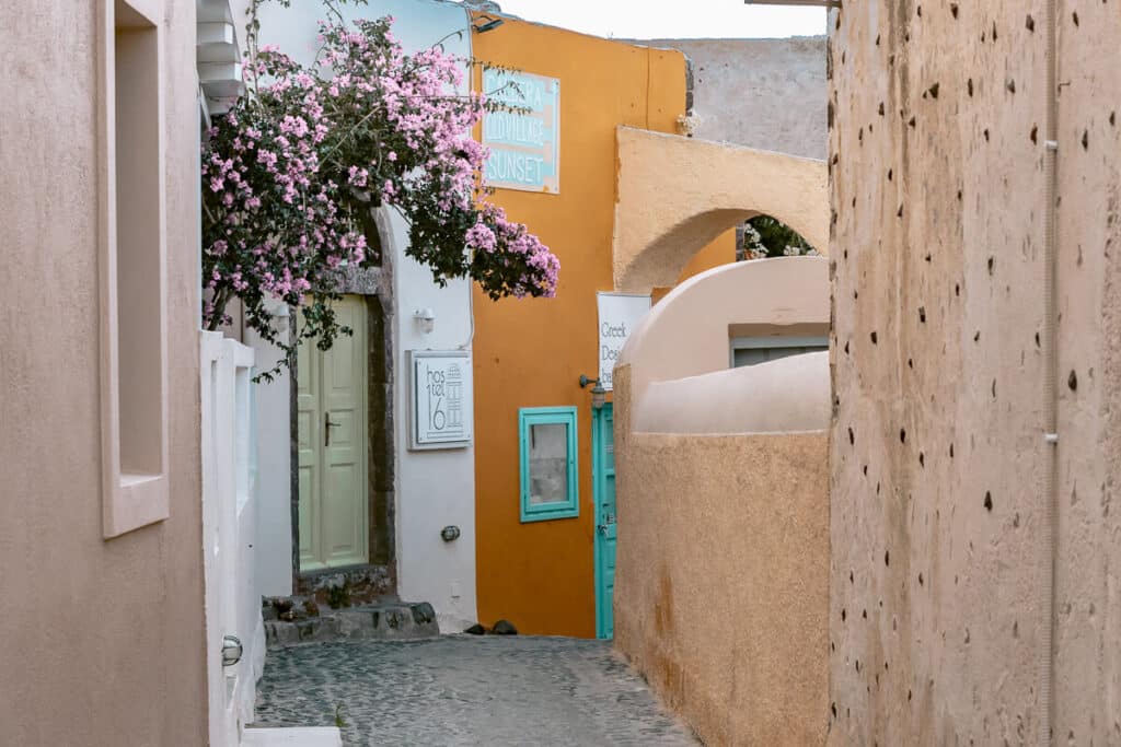 Stone alleyway in Santorini with textured walls and pops of turquoise and terracotta in a peaceful winter setting