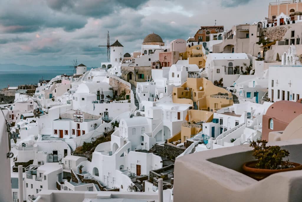 Wide panoramic view capturing multiple windmills and a large section of Oia’s architecture cascading down the cliffside.