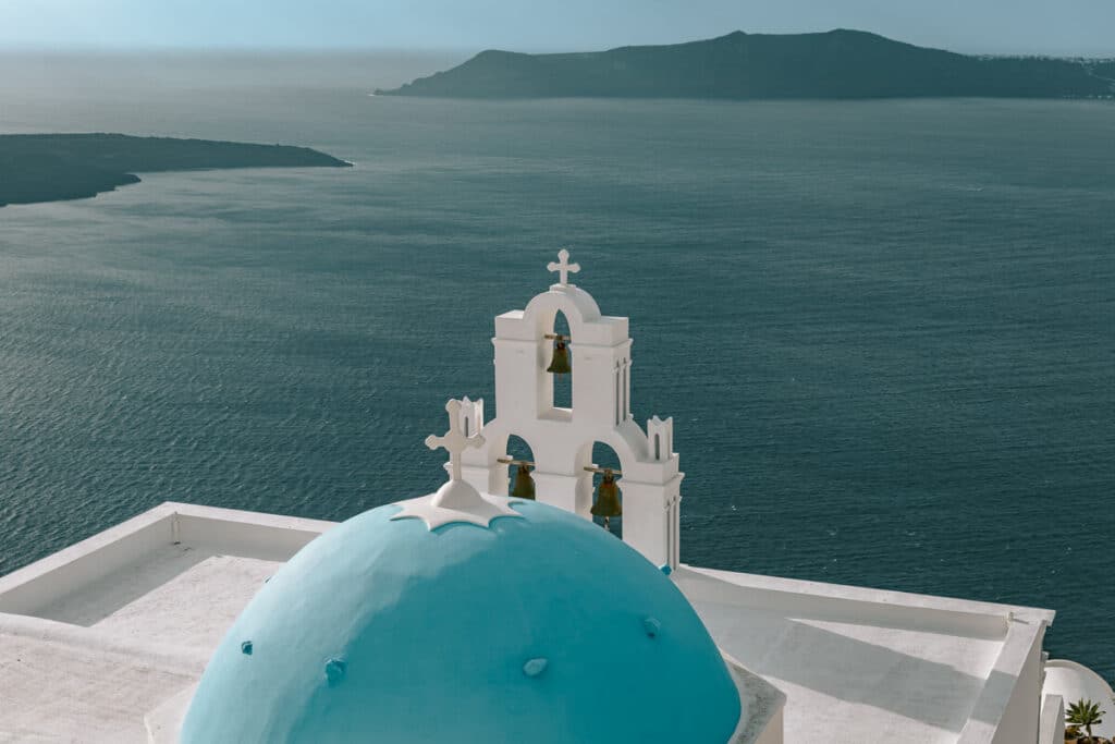 Iconic blue-domed church and bell tower overlooking the Aegean Sea in Santorini