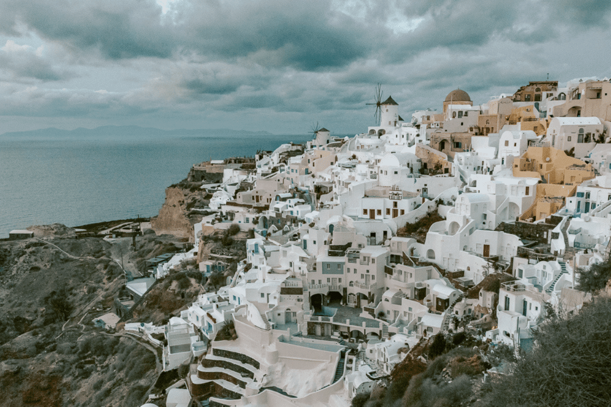 Whitewashed buildings and traditional windmills in Oia overlooking the Aegean Sea under dramatic clouds, featured in a collection of Santorini captions.