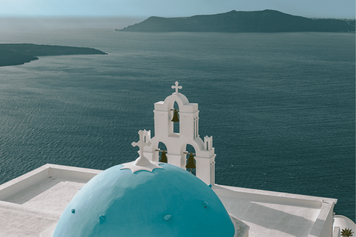 Santorini in winter view of a blue domed church and white bell tower overlooking the Aegean Sea.