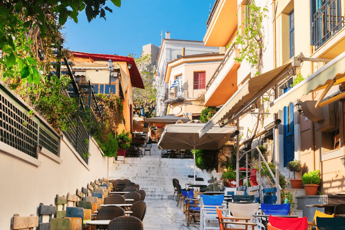 Solo travel to Athens street scene with colorful buildings, outdoor café seating, and sunny steps in a charming Athens neighborhood