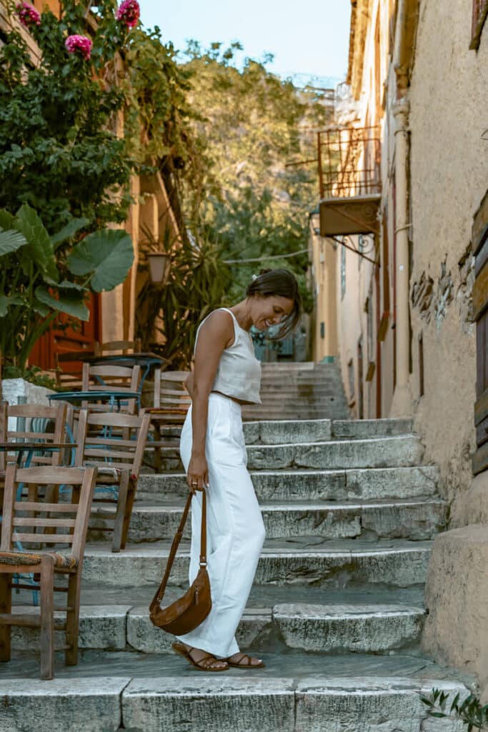 Me walking down a stone staircase in Athens’ Plaka neighborhood, surrounded by charming old buildings and blooming bougainvillea. Her light linen outfit blends with the warm tones of the alley, capturing a slow, reflective travel moment.