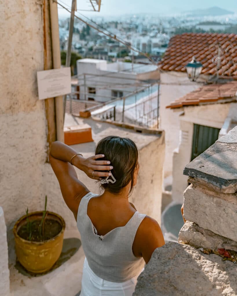 Me with my back to the camera, a woman stands on a balcony in Anafiotika, hand in her hair, gazing out at the sweeping view of Athens’ rooftops. The mix of sun-washed walls and terracotta tiles frames this quiet, reflective moment on a solo adventure.
